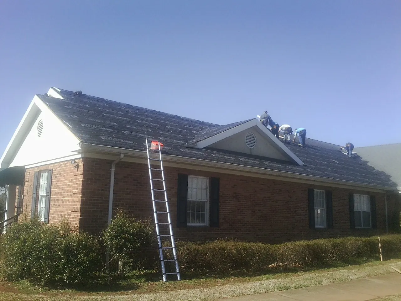 Crew tearing shingles off a brick ranch roof with a ladder set — Emergency Roof Repair work by our crew in Jefferson City