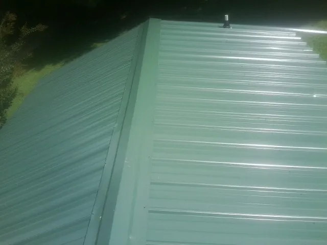 New green metal panels meeting at the ridge of a roof — Flat Roof Repair work by our crew in Jefferson City