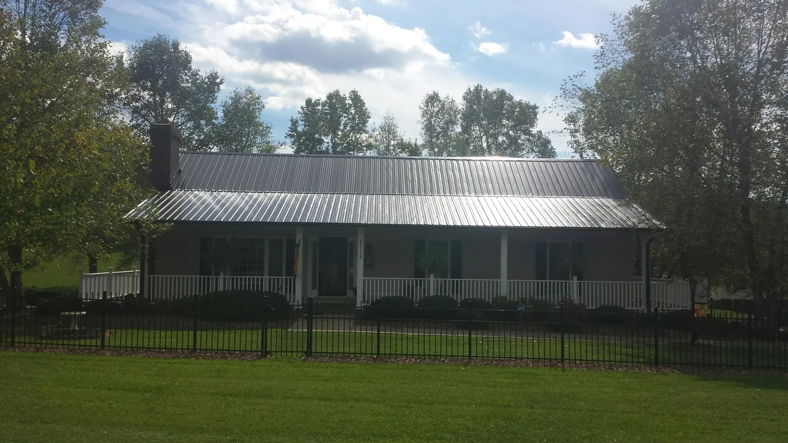 Gray metal roof on a brick ranch with a full width front porch — Gutter Guard Installation work by our crew in Jefferson City